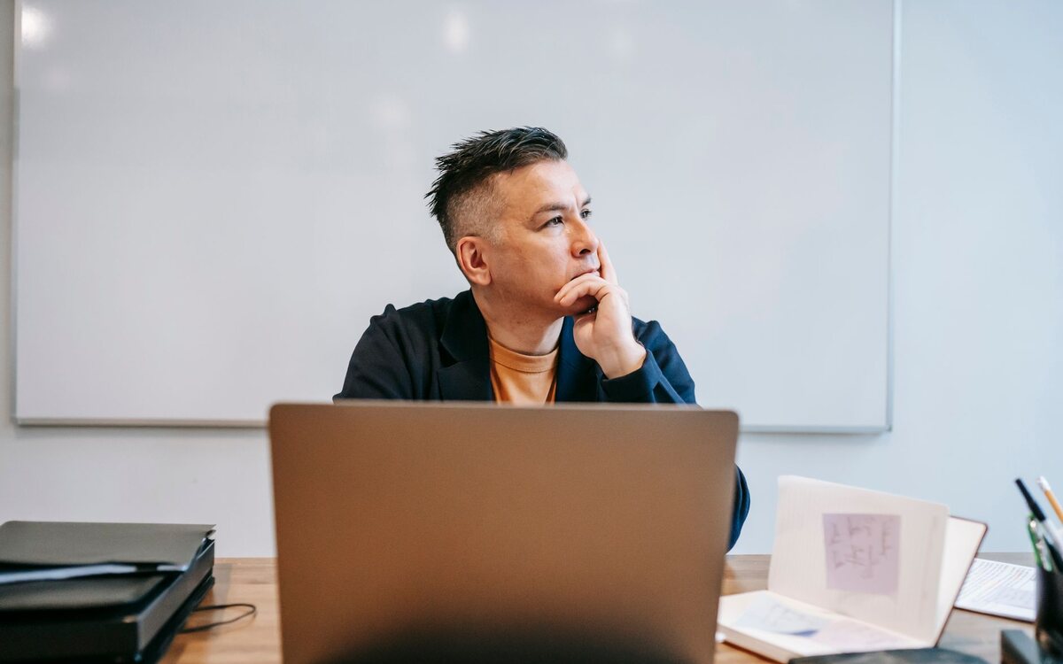 Man at his desk looking thoughtfully at a laptop